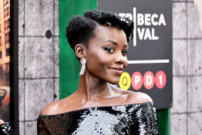 Lupita Nyong&#x27;o, in an off-shoulder sequined dress, poses in front of a Tribeca Festival sign