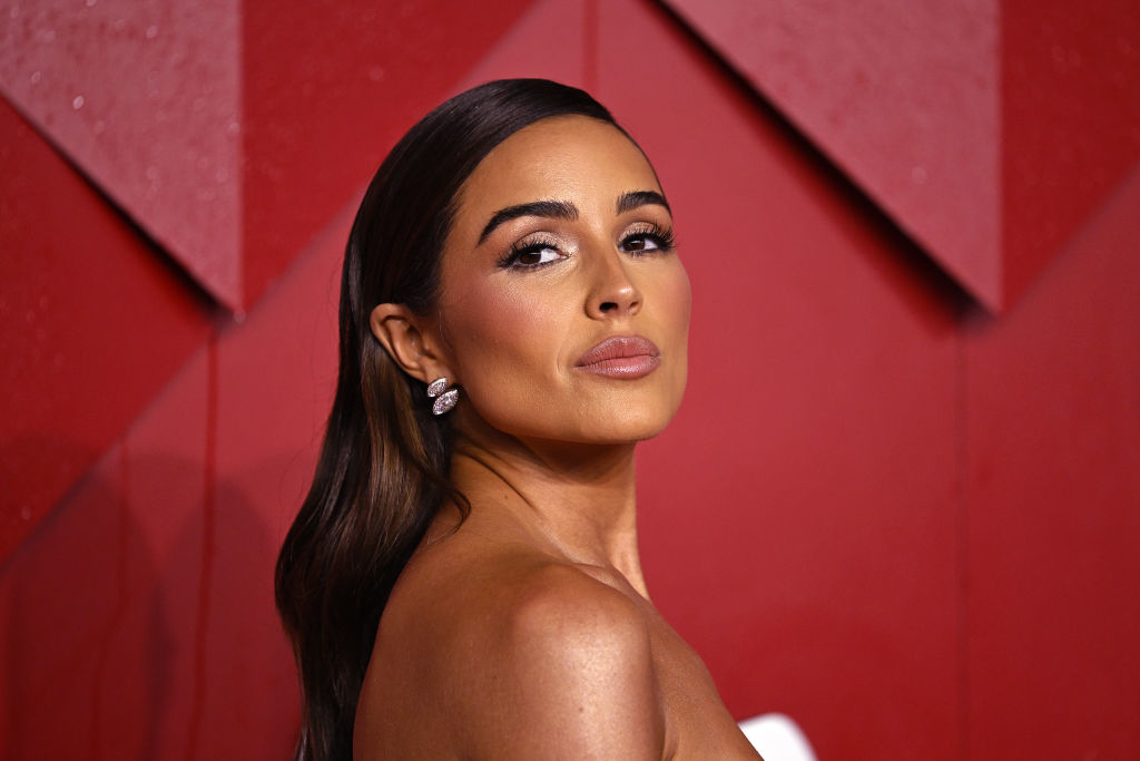 Olivia Culpo posing on a red carpet, wearing an elegant strapless gown with diamond earrings
