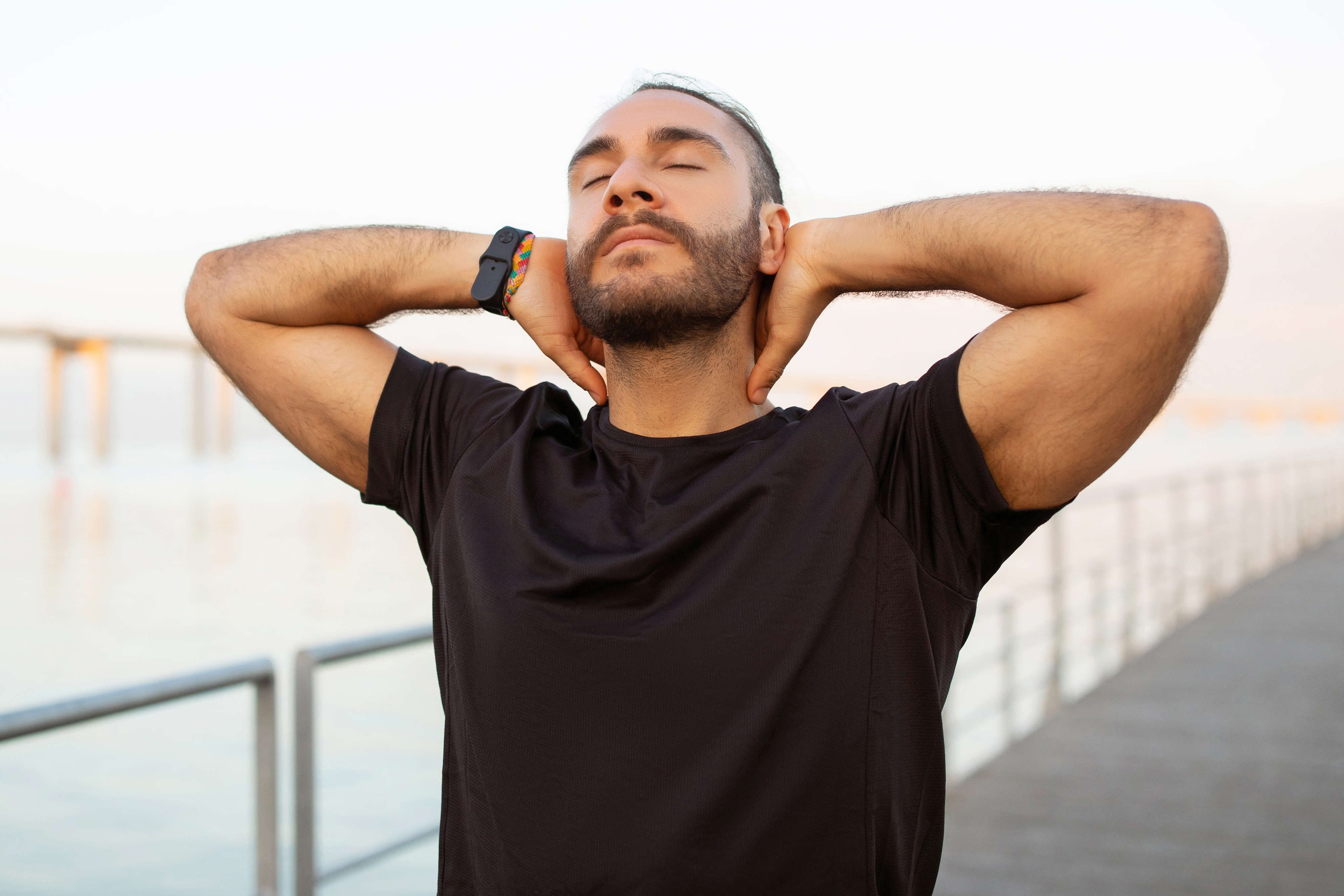 A person with eyes closed and arms behind their head relaxes by an outdoor waterfront railing