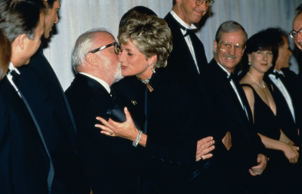 I don&#x27;t know who the people in the image are. A woman in an elegant dress kisses a man on the cheek while others in formal attire stand in the background