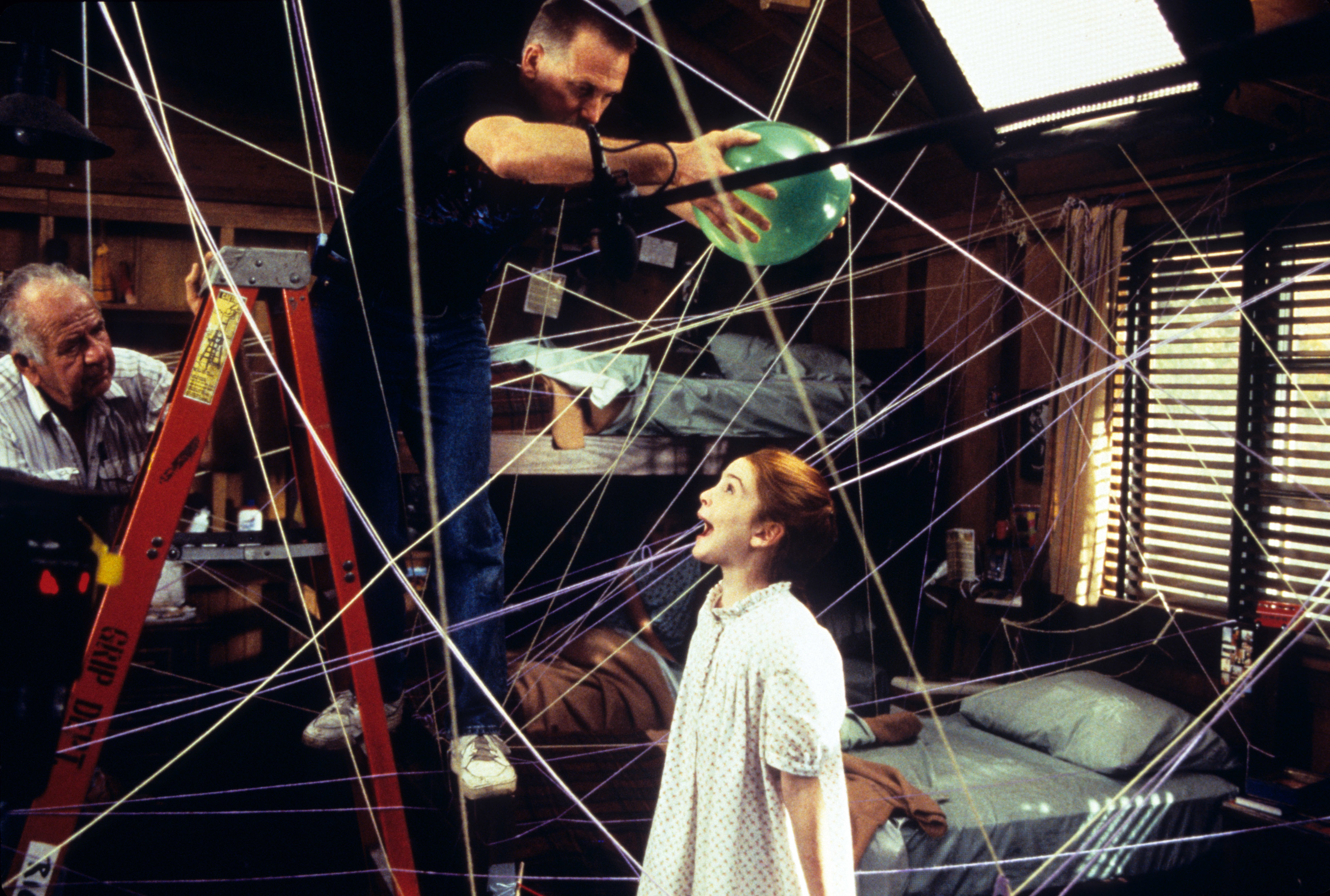 Dana Carvey and young Juliette Brewer in a behind-the-scenes moment from the film &quot;Clean Slate,&quot; with a crew member adjusting a green balloon in a web of strings