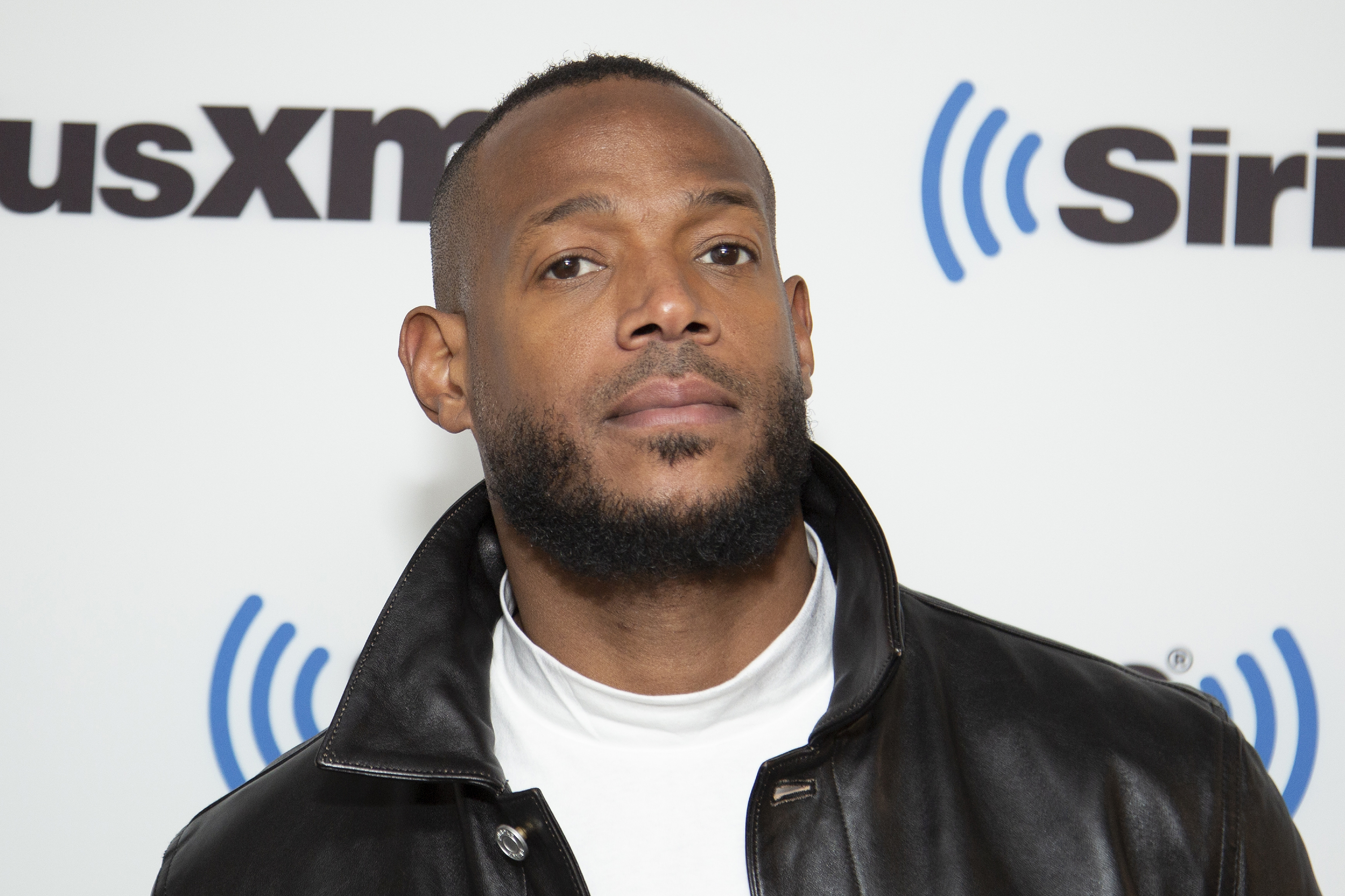 Marlon Wayans at a SiriusXM event, wearing a black leather jacket over a white turtleneck