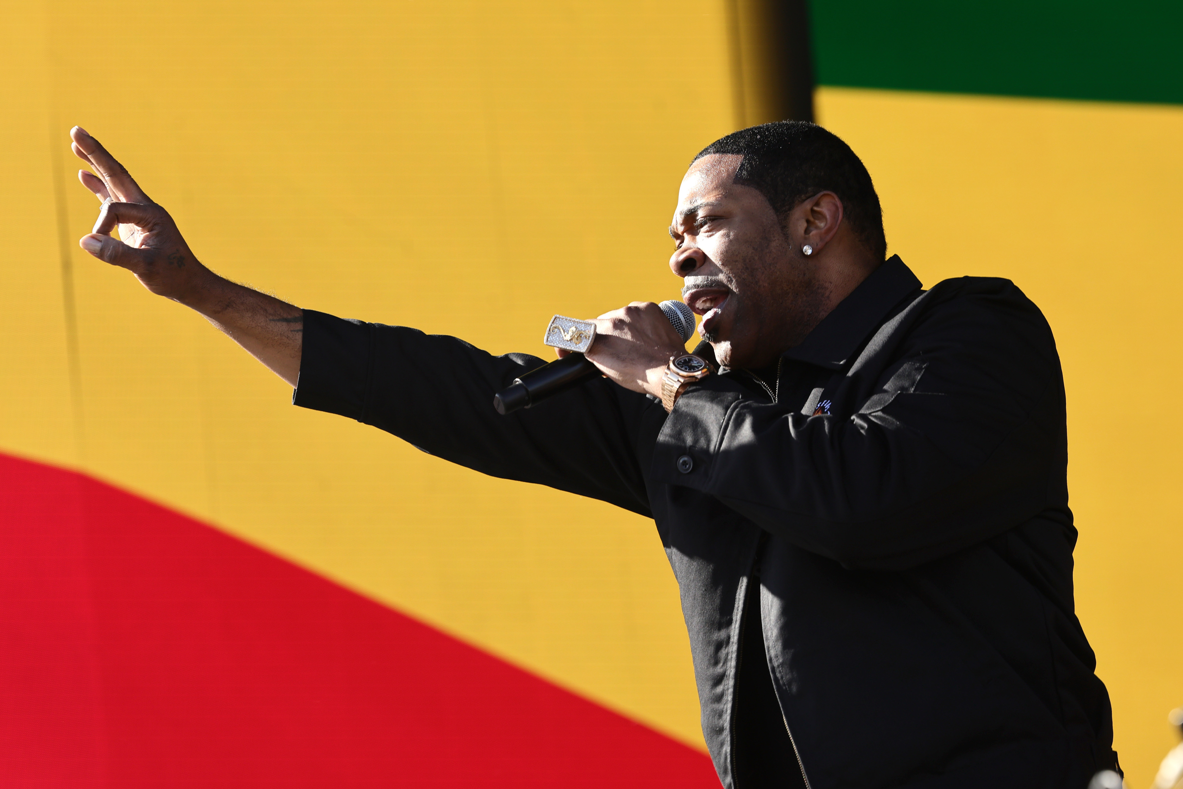 Busta Rhymes performs passionately on stage, holding a microphone and gesturing towards the audience