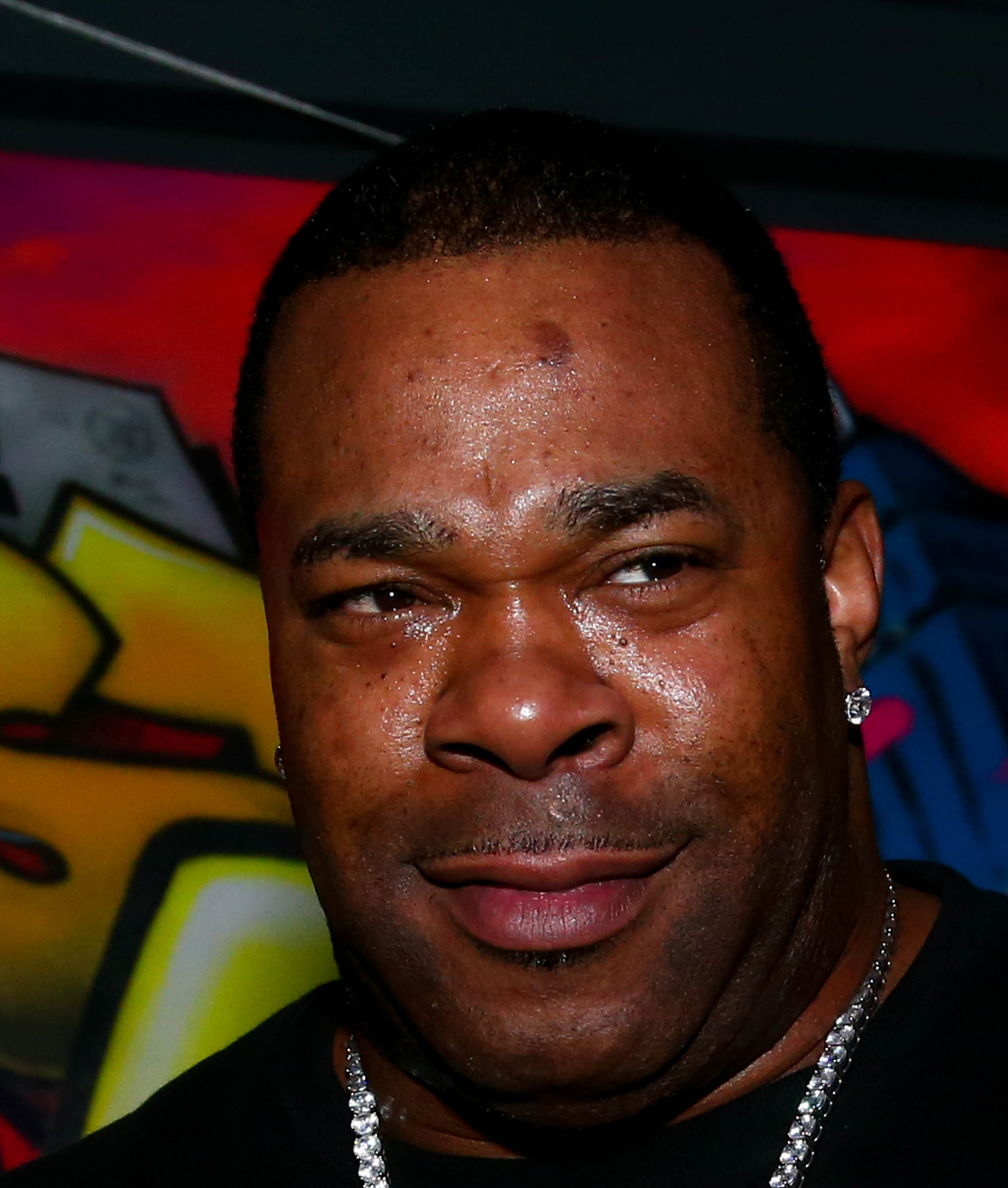 Close-up of Busta Rhymes at an event, wearing diamond earrings and a necklace