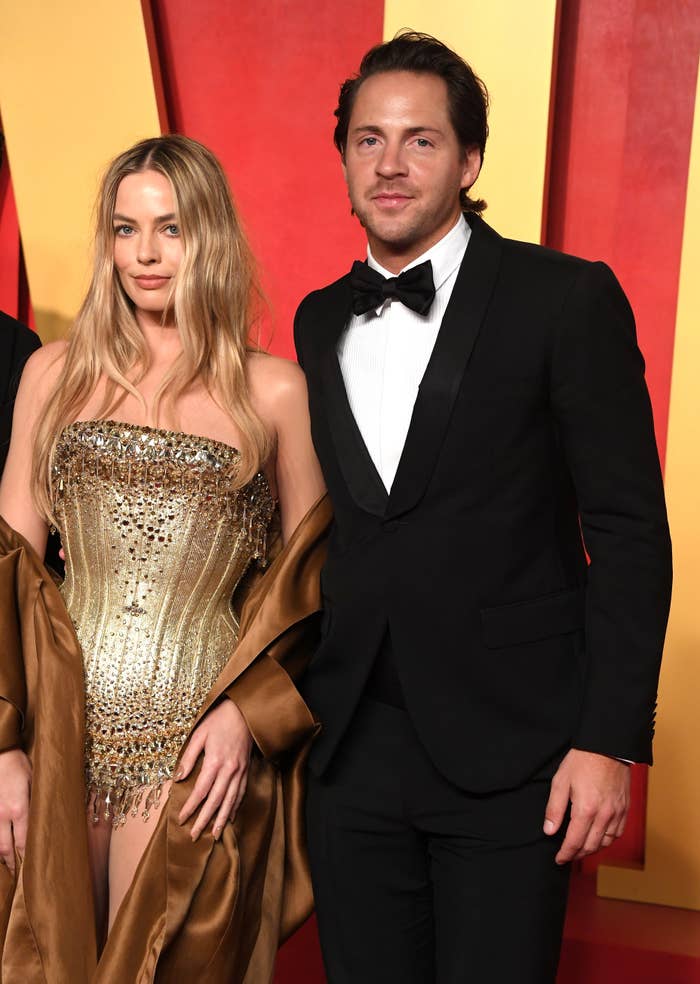 Margot Robbie in an embellished strapless dress and Tom Ackerley in a black tuxedo on the red carpet