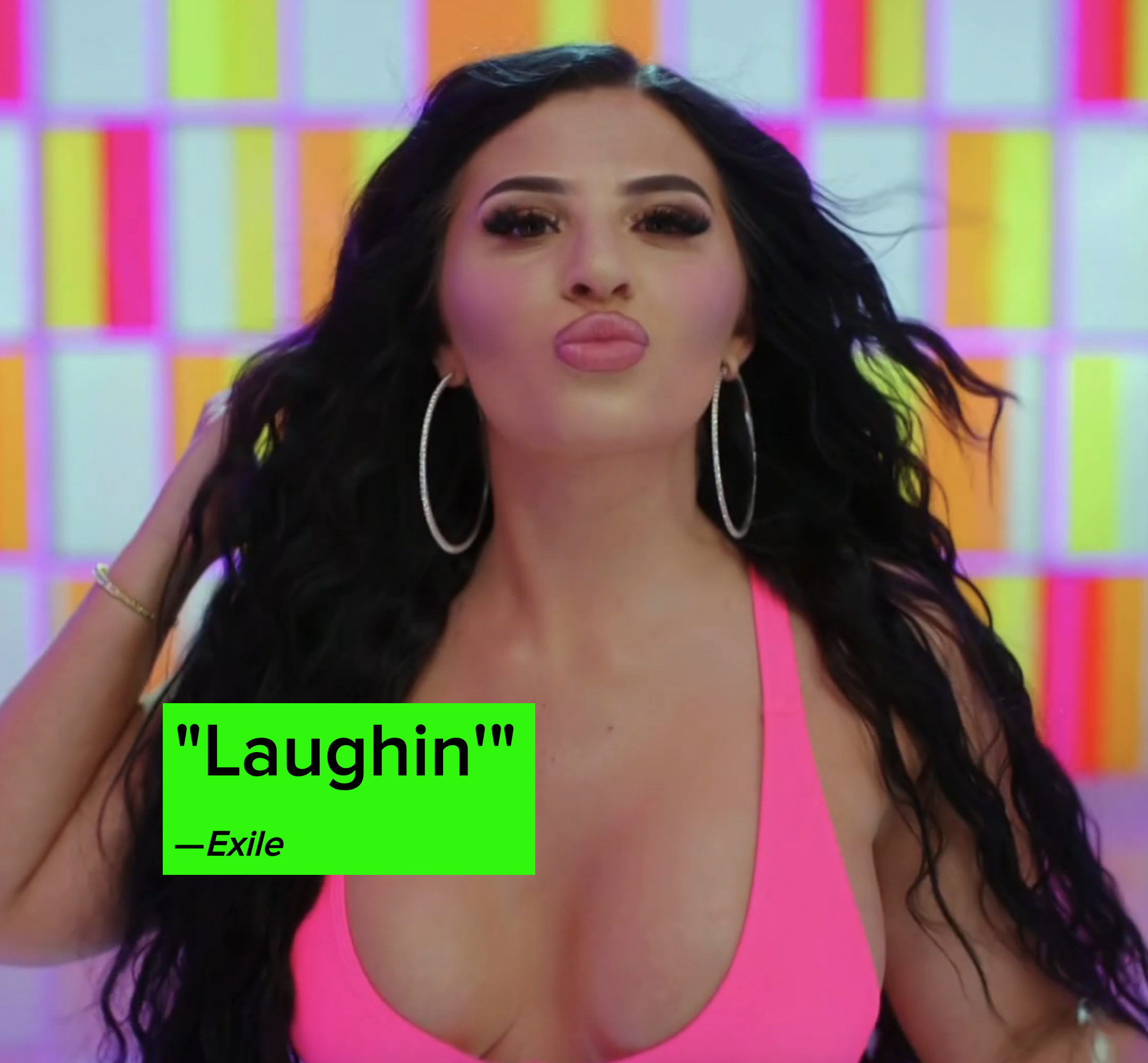 Hannah with long wavy black hair and large hoop earrings, poses against a colorful background, wearing a low-cut top