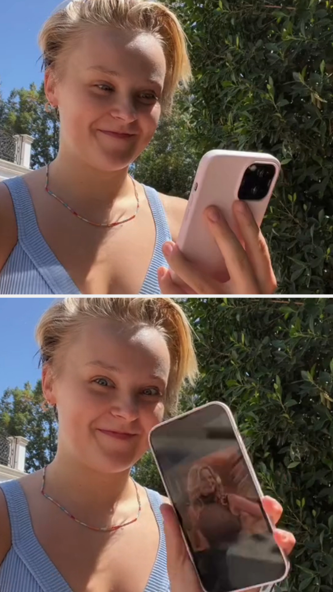 JoJo Siwa, wearing a sleeveless top, smiles while holding a smartphone with a picture of Candace Cameron Bure on the screen