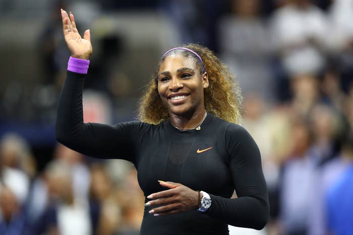 Serena Williams waves and smiles while wearing a sleek athletic outfit on the tennis court