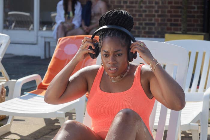 Queenie is sitting poolside wearing a swimsuit and headphones, adjusting them with a focused expression