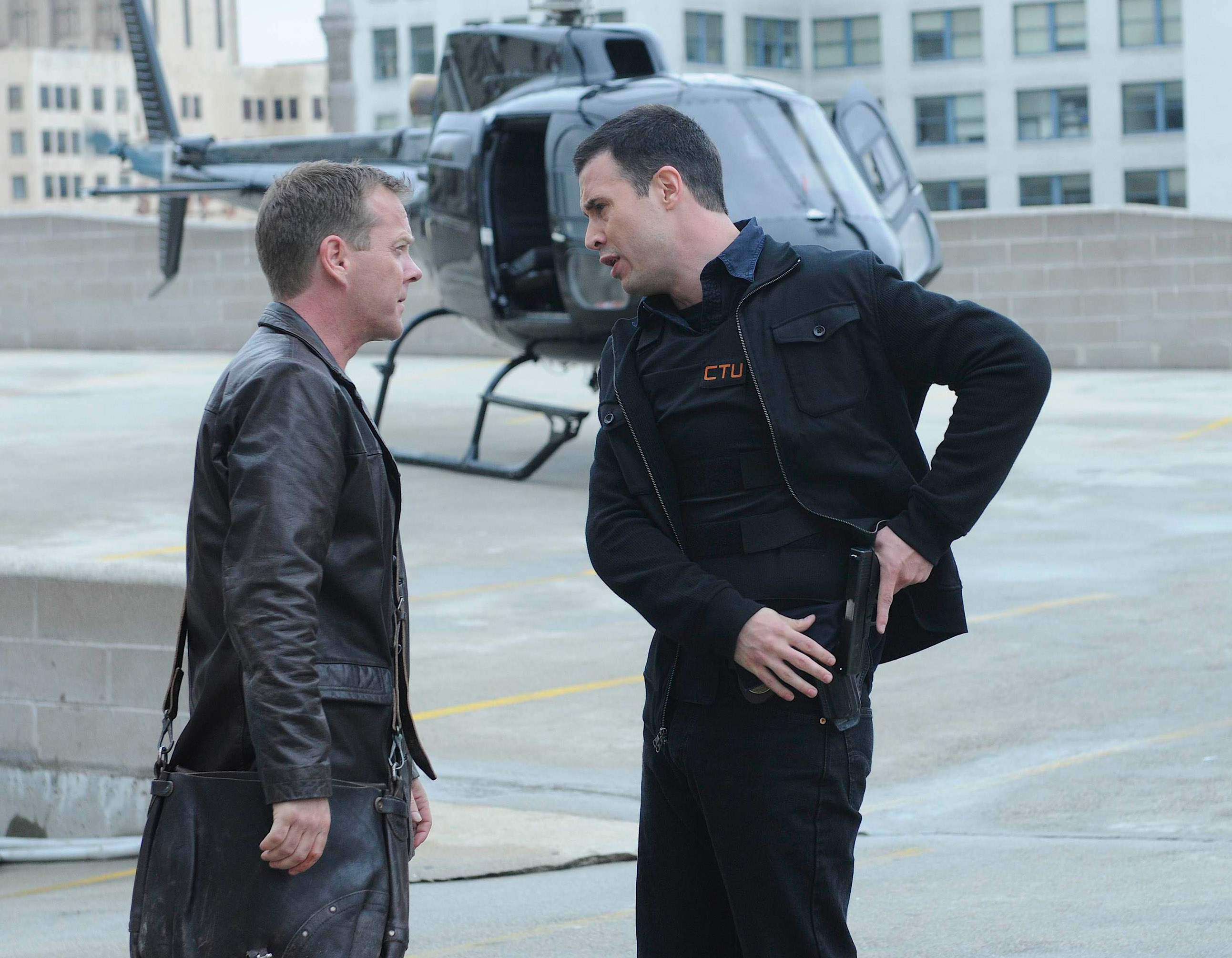 Kiefer Sutherland and Freddie Prinze Jr. in a scene from &quot;24,&quot; standing on a rooftop with a helicopter in the background. Sutherland wears a leather jacket