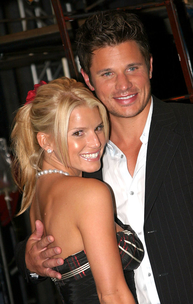 Jessica Simpson and Nick Lachey are smiling and posing closely, with Jessica in a strapless dress and pearl necklace, and Nick in a suit with an open-collared shirt