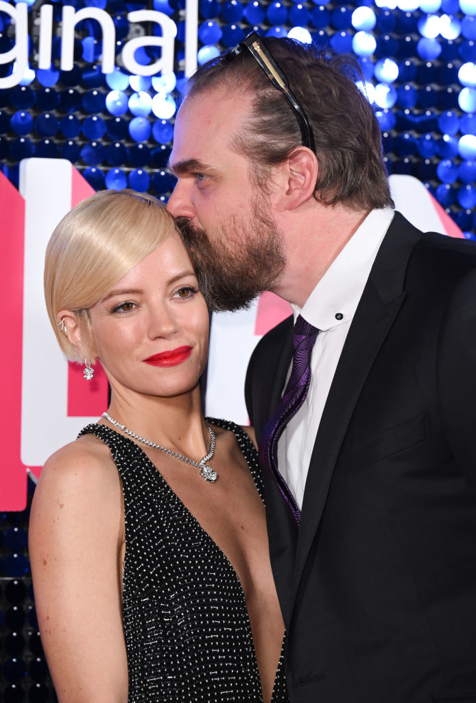 David Harbour wearing a black suit kisses Lily Allen on the head on a red carpet; Lily wears a sparkling dress