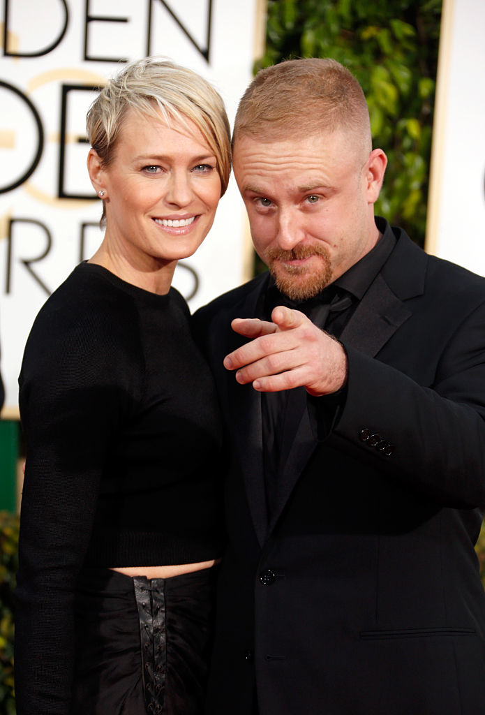 Robin Wright and Ben Foster pose together on the red carpet, with Robin in an elegant black dress and Ben in a black suit, pointing toward the camera