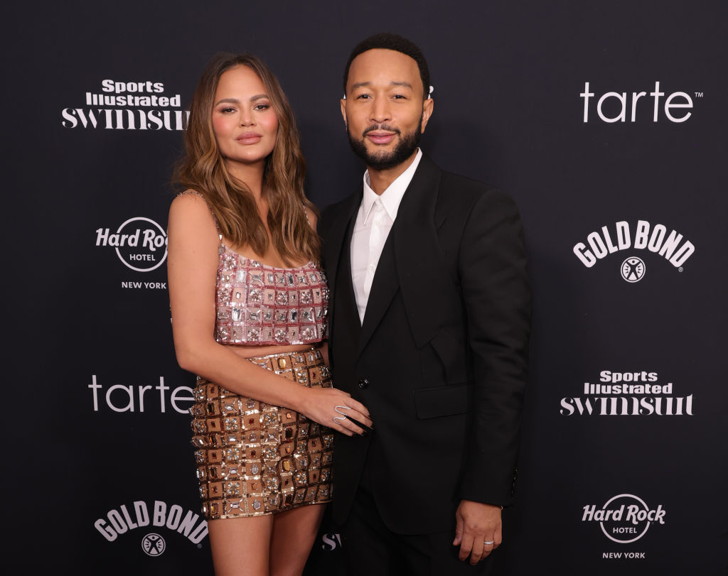 Chrissy Teigen and John Legend on the red carpet at a Sports Illustrated event. Chrissy wears a bejeweled top and skirt, while John wears a black suit
