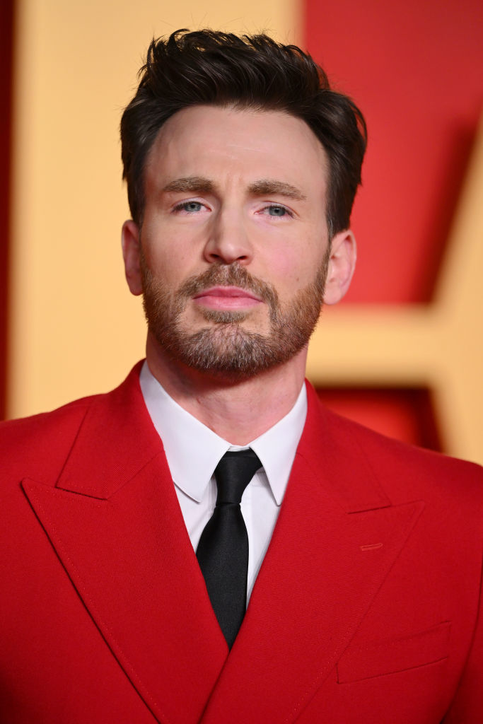 Chris Evans on the red carpet in a red suit with a black tie