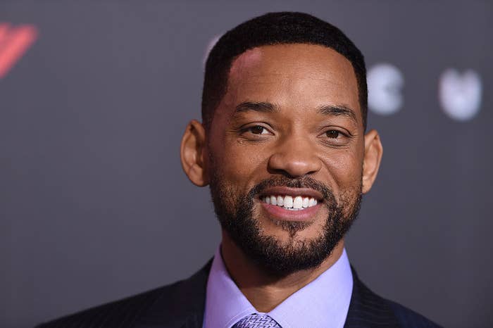 Will Smith smiles at a red carpet event, wearing a classic suit with a light-colored shirt