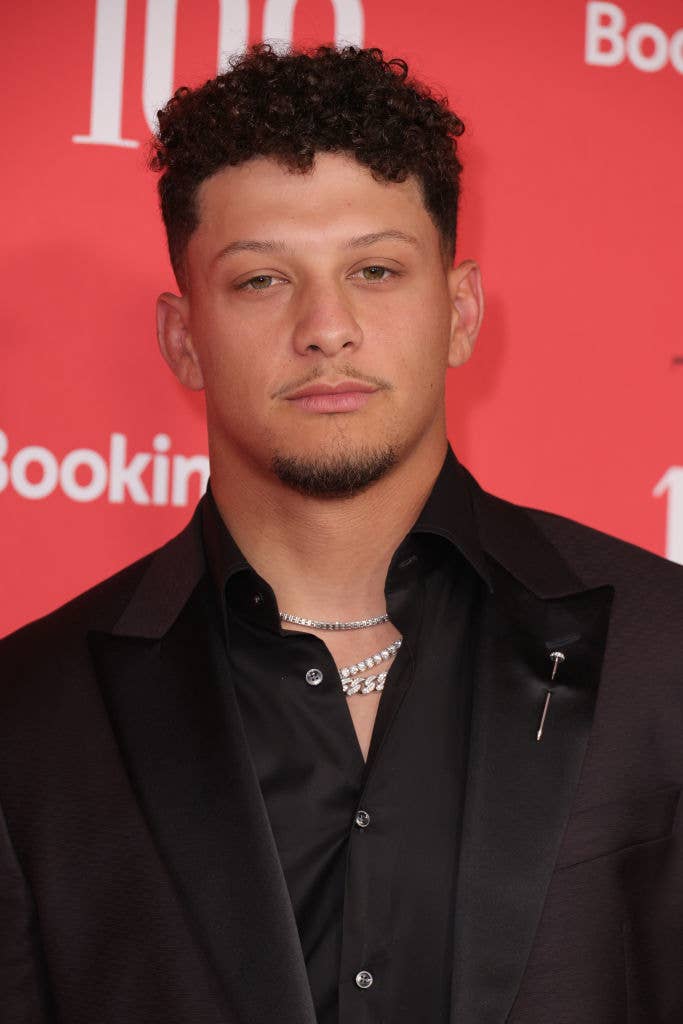 Patrick Mahomes at an event, dressed in a black suit and shirt with chain necklaces, against a red background with text