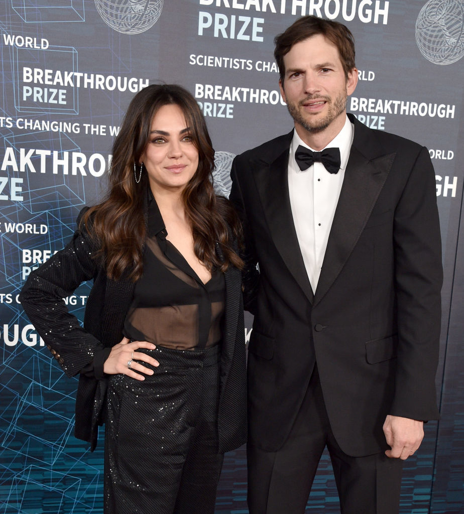 Mila Kunis and Ashton Kutcher are on the red carpet at the Breakthrough Prize event. Mila is wearing a stylish black outfit, and Ashton is in a classic black tuxedo