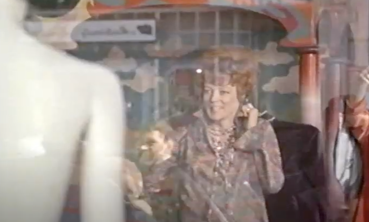 A person dressed in vintage-style clothing holds a phone to their ear, smiling. The background features a store with a retro vibe and a mannequin in the foreground