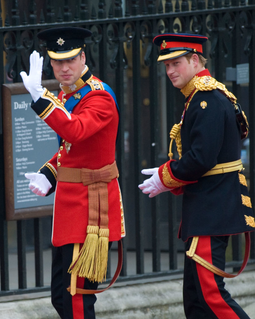 Prince William and Prince Harry in formal military uniforms wave to the crowd outside a historical building