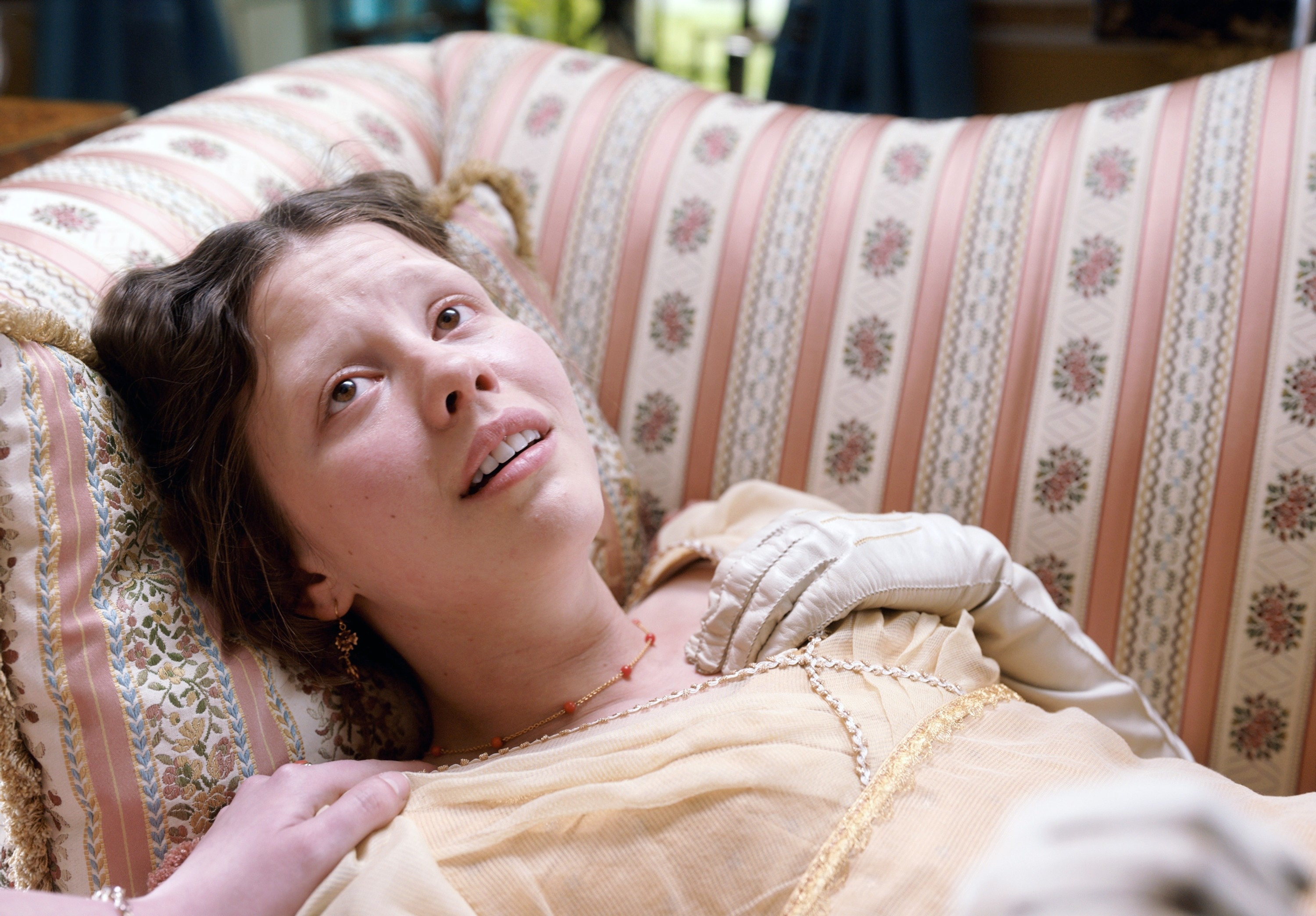 Mia Goth on a patterned couch in a scene from &quot;Emma&quot;