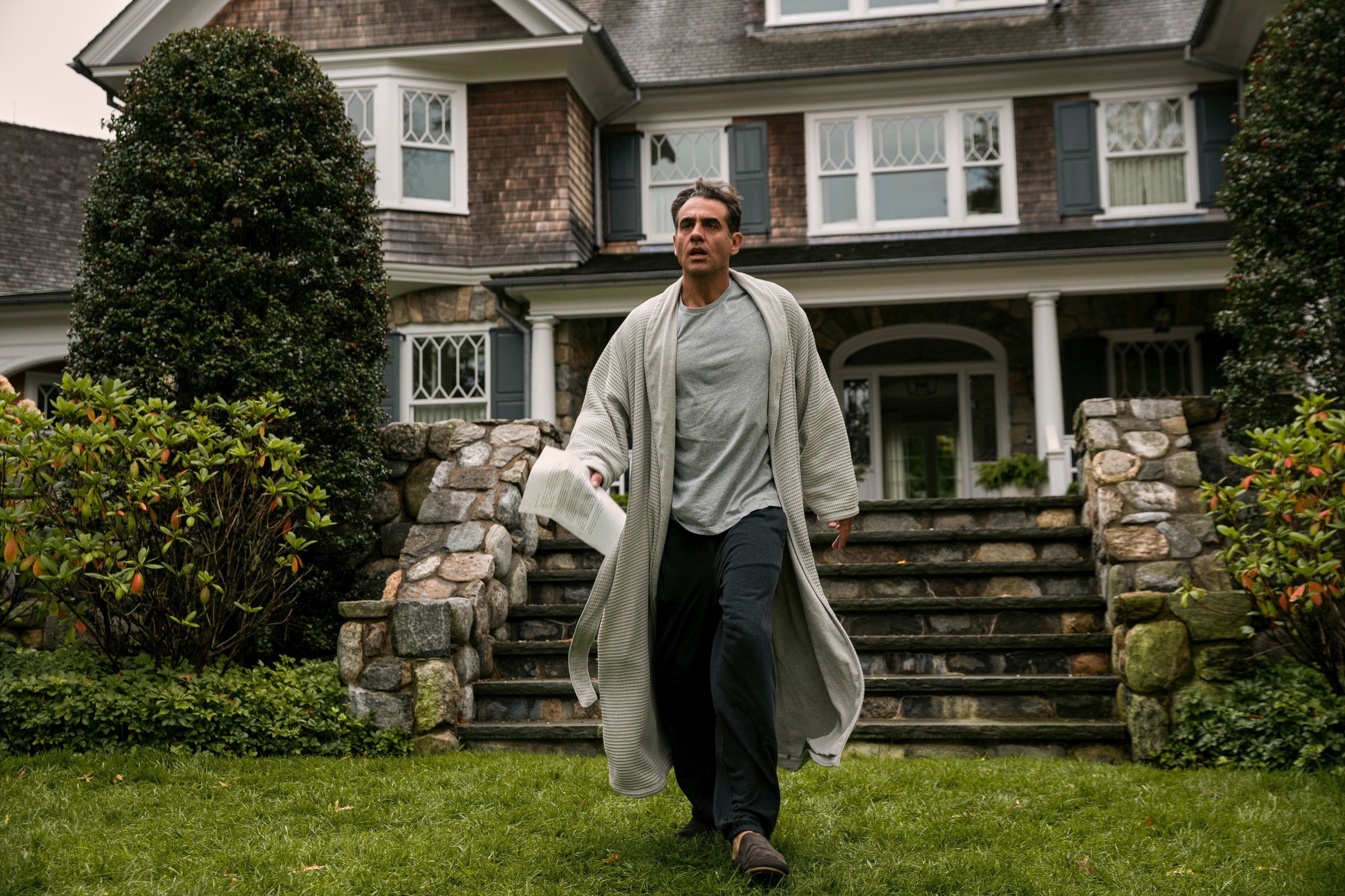 Bobby Cannavale in a robe and PJs walking outside as he holds a piece of paper in a scene from &quot;The Watcher&quot;
