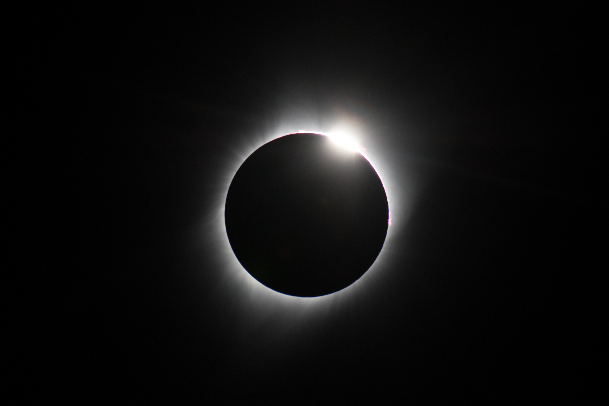 A total solar eclipse captured with the moon completely covering the sun, except for a bright light peeking out from the edge