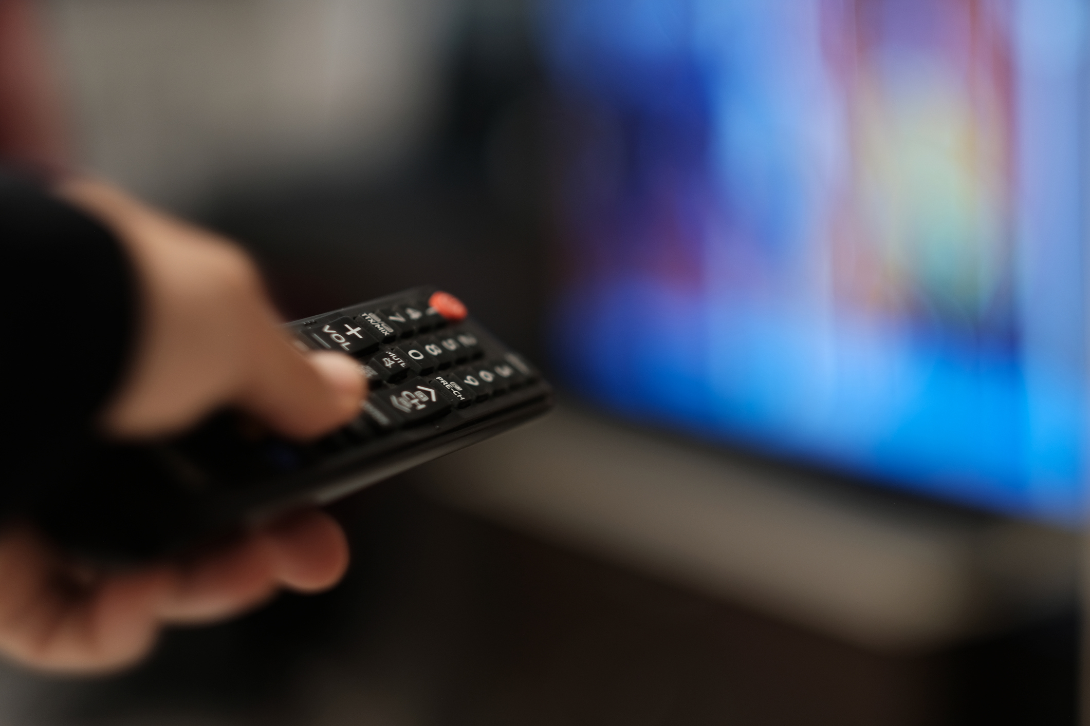 A person holds a remote control pointed at a blurred television screen