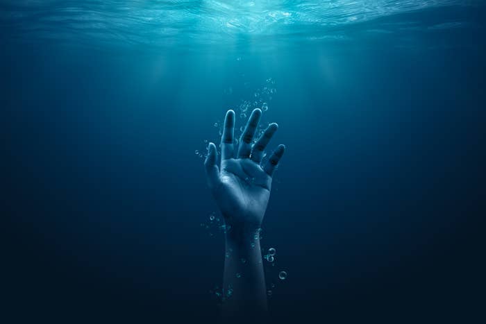 A single hand reaching out from underwater toward the surface, with light filtering down from above