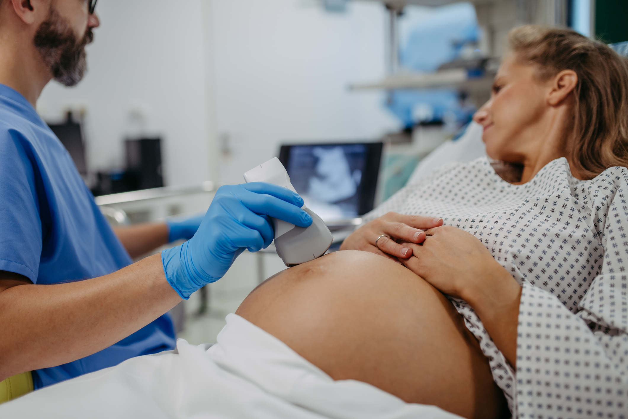 A doctor performs an ultrasound on a pregnant patient&#x27;s abdomen while she lies on an examination bed in a medical setting