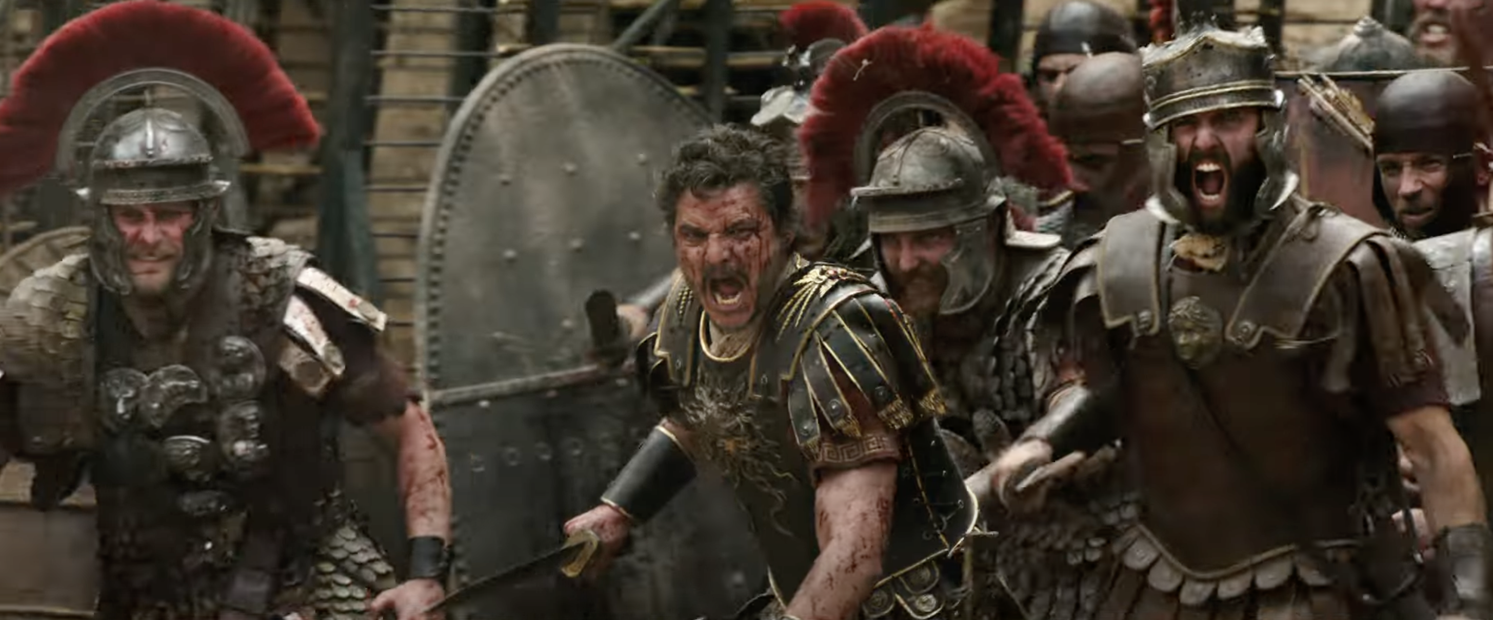 Scene from a historical film featuring actors in Roman soldier costumes, brandishing weapons and shields in the midst of battle