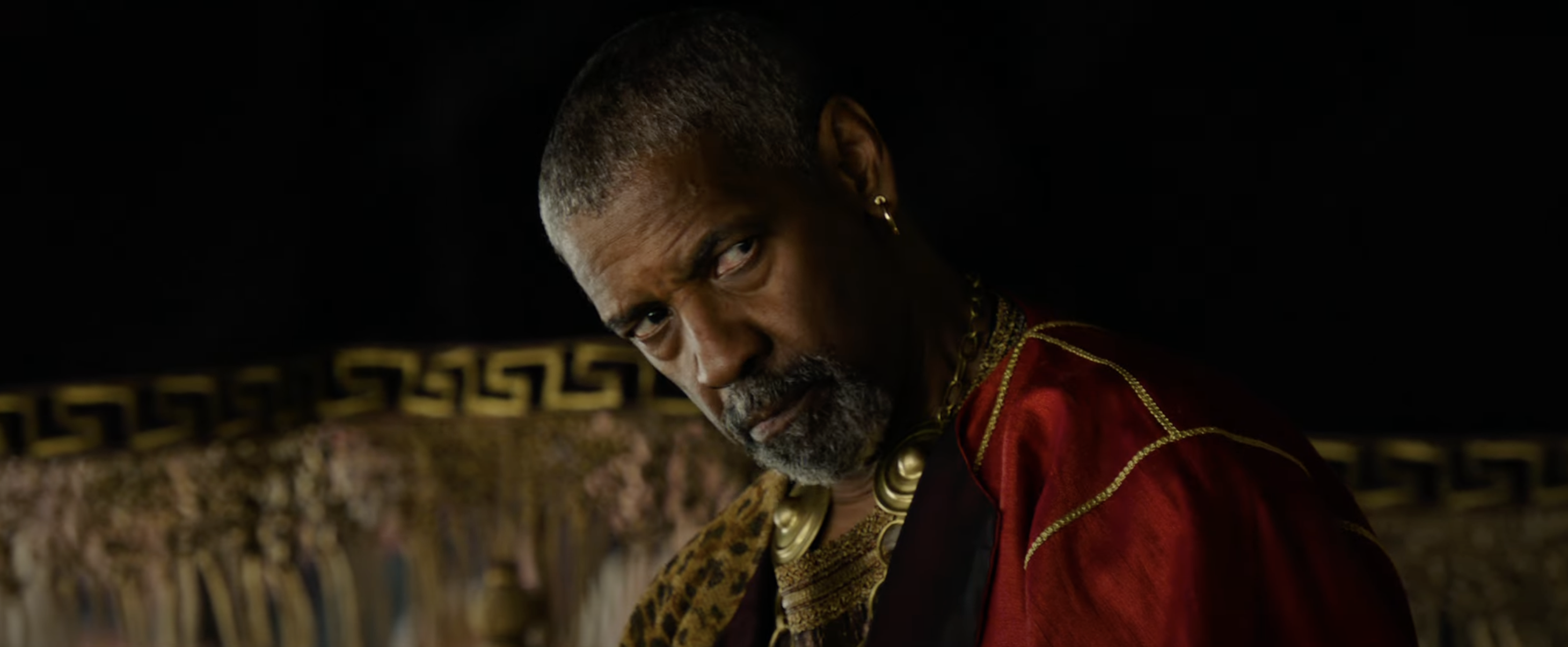 Denzel Washington in a scene, wearing regal attire with elaborate gold details, looking intensely with a serious expression