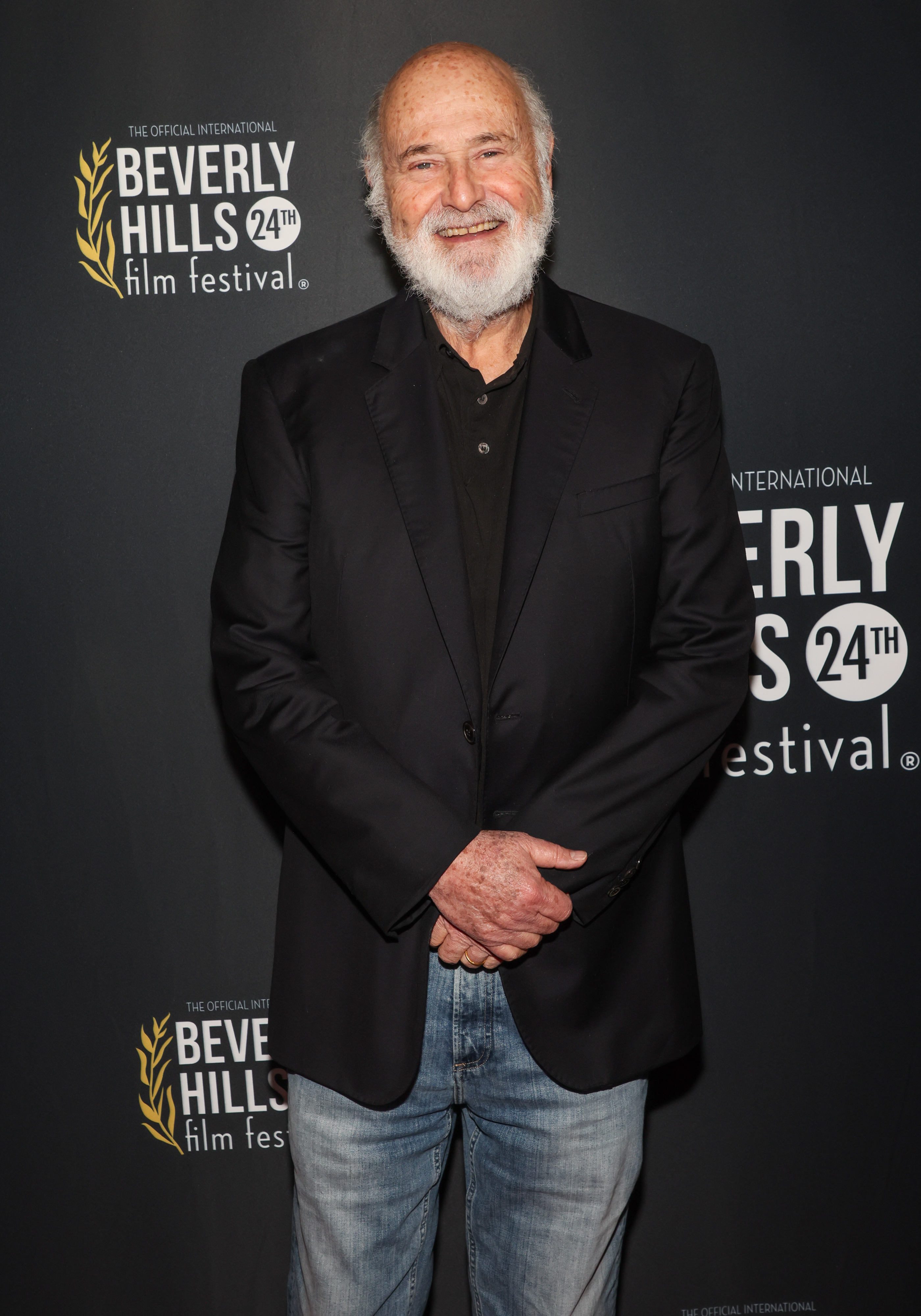 Rob Reiner smiles while posing in a dark blazer and jeans at the 24th Beverly Hills Film Festival