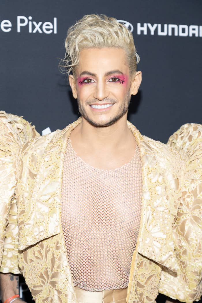 Frankie Grande at an event, wearing a lace jacket over a mesh top, with bright makeup and styled hair