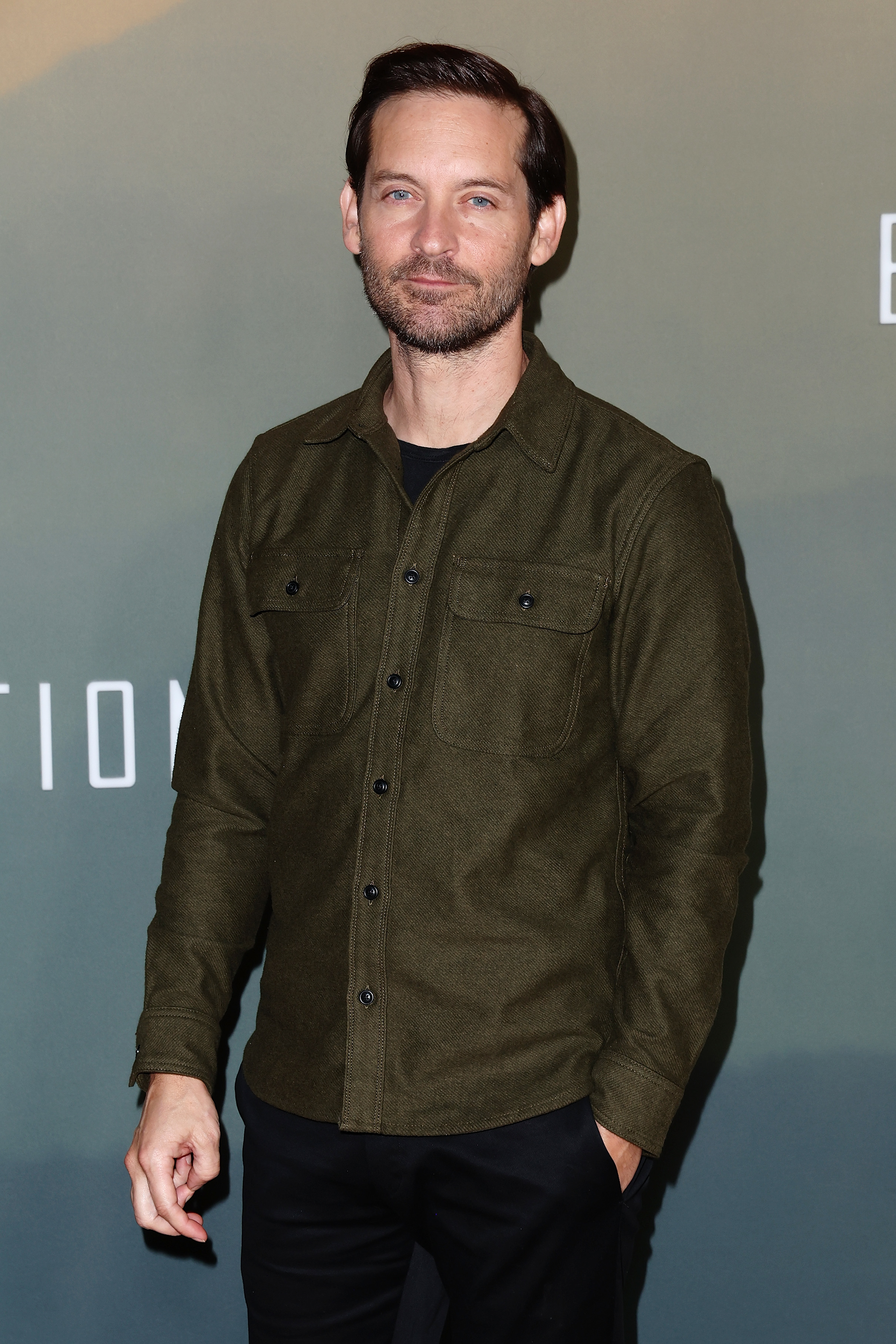 Tobey Maguire posing in a casual button-up shirt and pants at a press event