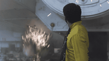 Donald Glover, wearing a yellow shirt and black tie, looks at sparking machinery in a scene from &quot;Solo: A Star Wars Story.&quot;