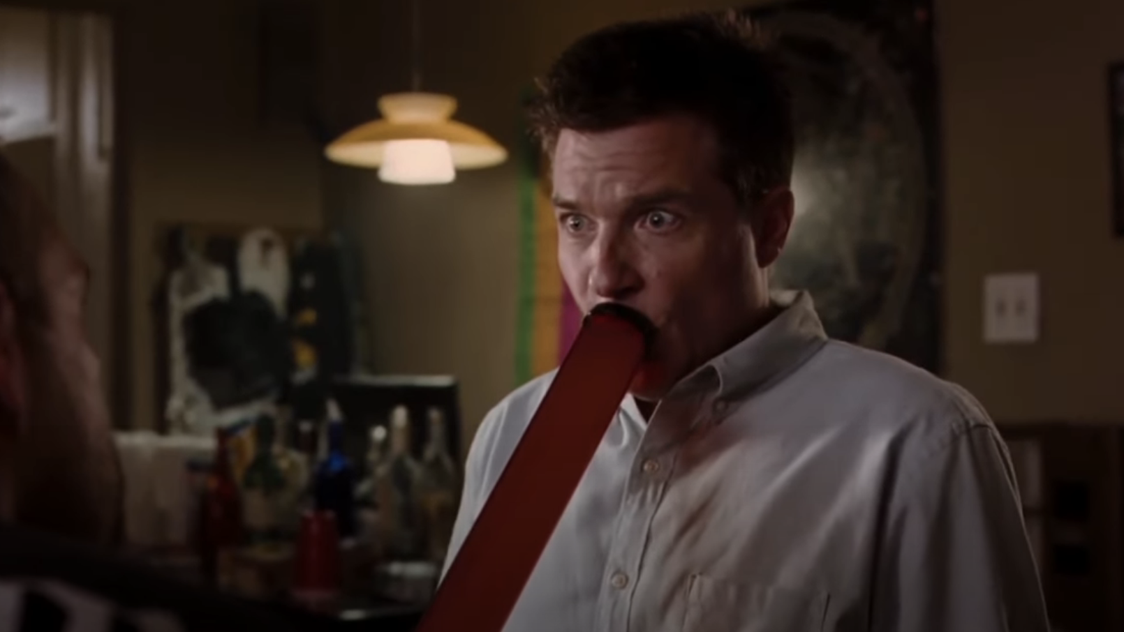 Jason Bateman with a large flat object in his mouth, appearing startled in a scene from a movie