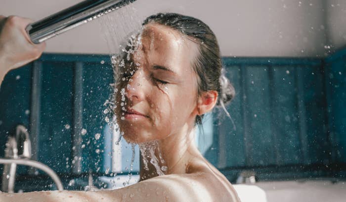 A woman with closed eyes enjoys a refreshing shower, water droplets splashing on her face