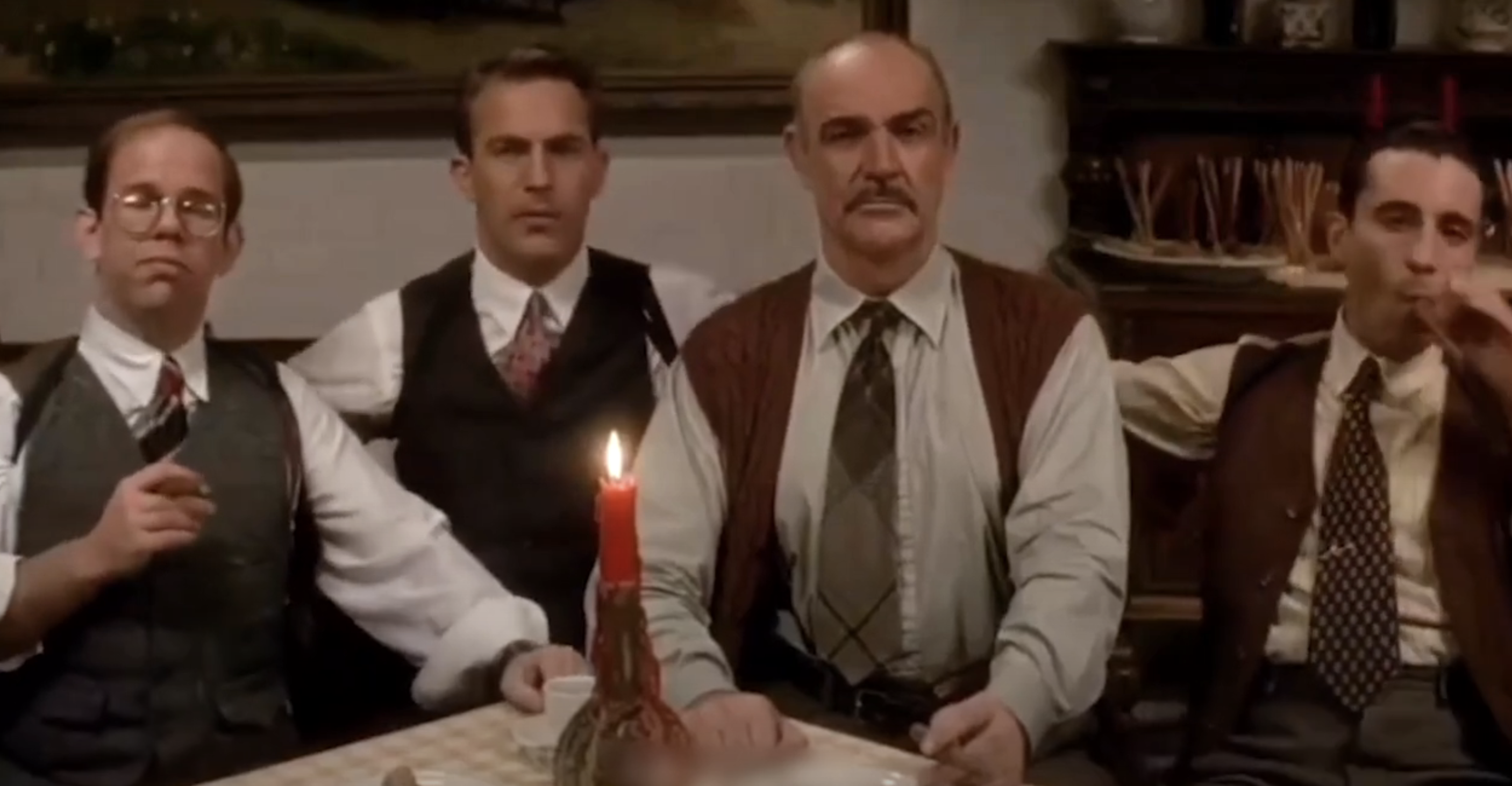 People in 1920s attire, sitting at a table with a burning candle. From left to right: a man with glasses, Kevin Costner, Sean Connery, and another man smoking a cigar