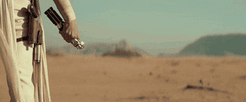 Rey holds a lightsaber, standing in a desert setting from Star Wars: The Rise of Skywalker