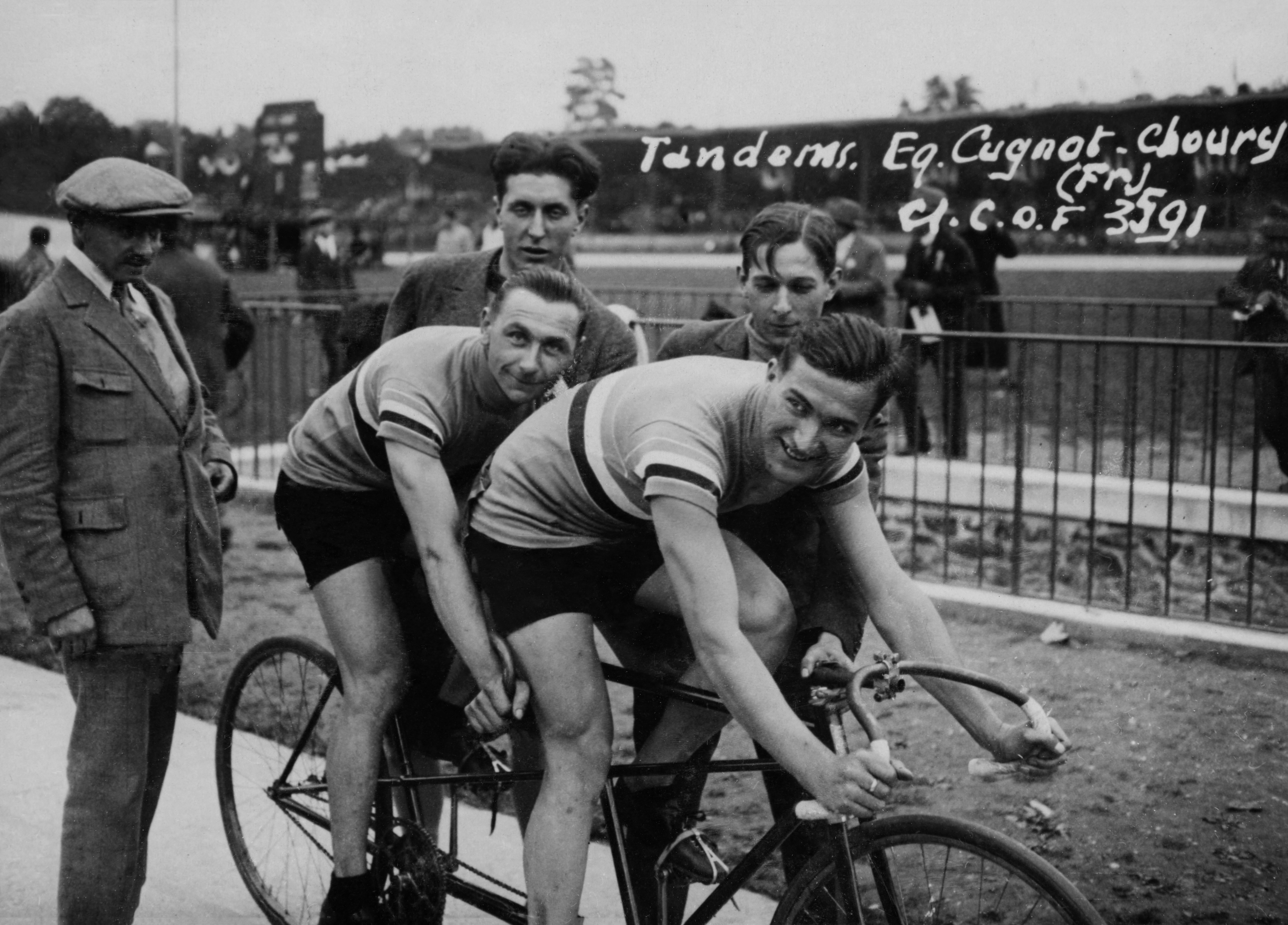 Three cyclists and two onlookers on a tandem bike at a sports event. Sign reads, &quot;Tandems, Eq. Cugnot-Choury (Fr.), G.C. o. F 391.&quot;