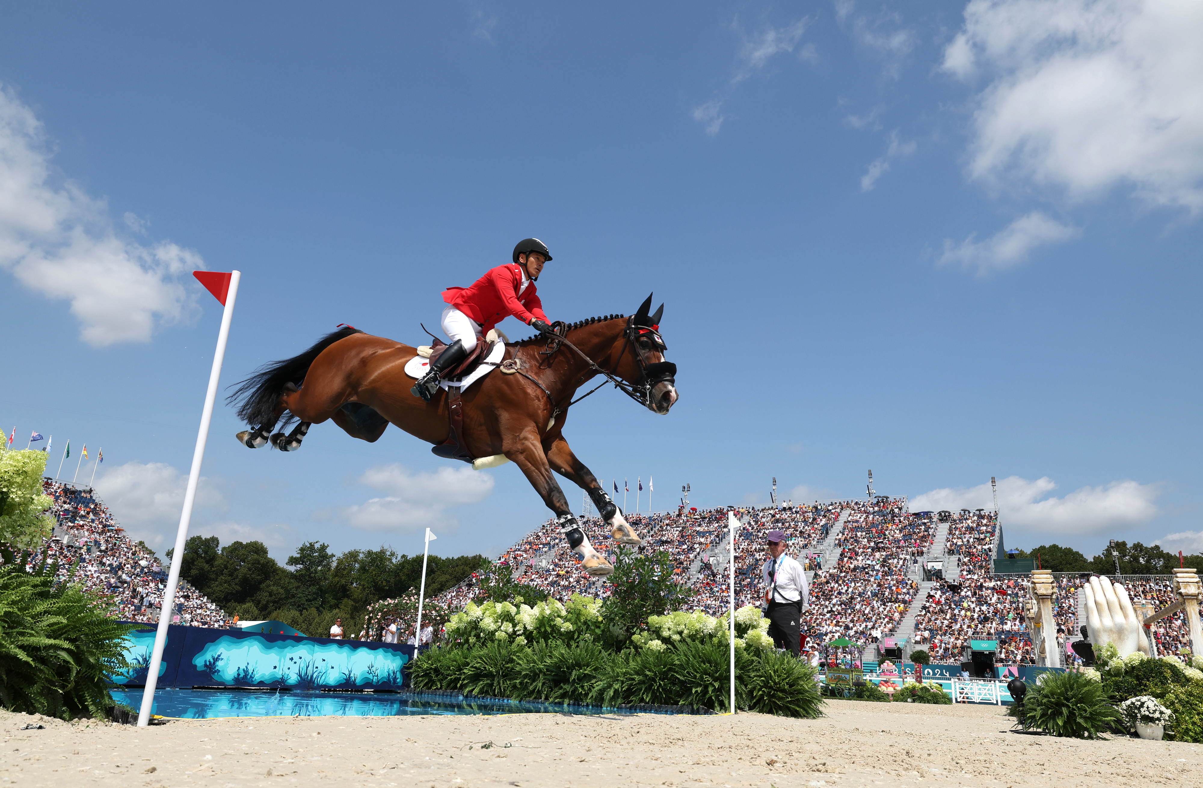 An equestrian rider in competition, mid-air over a jump with the crowd in the background