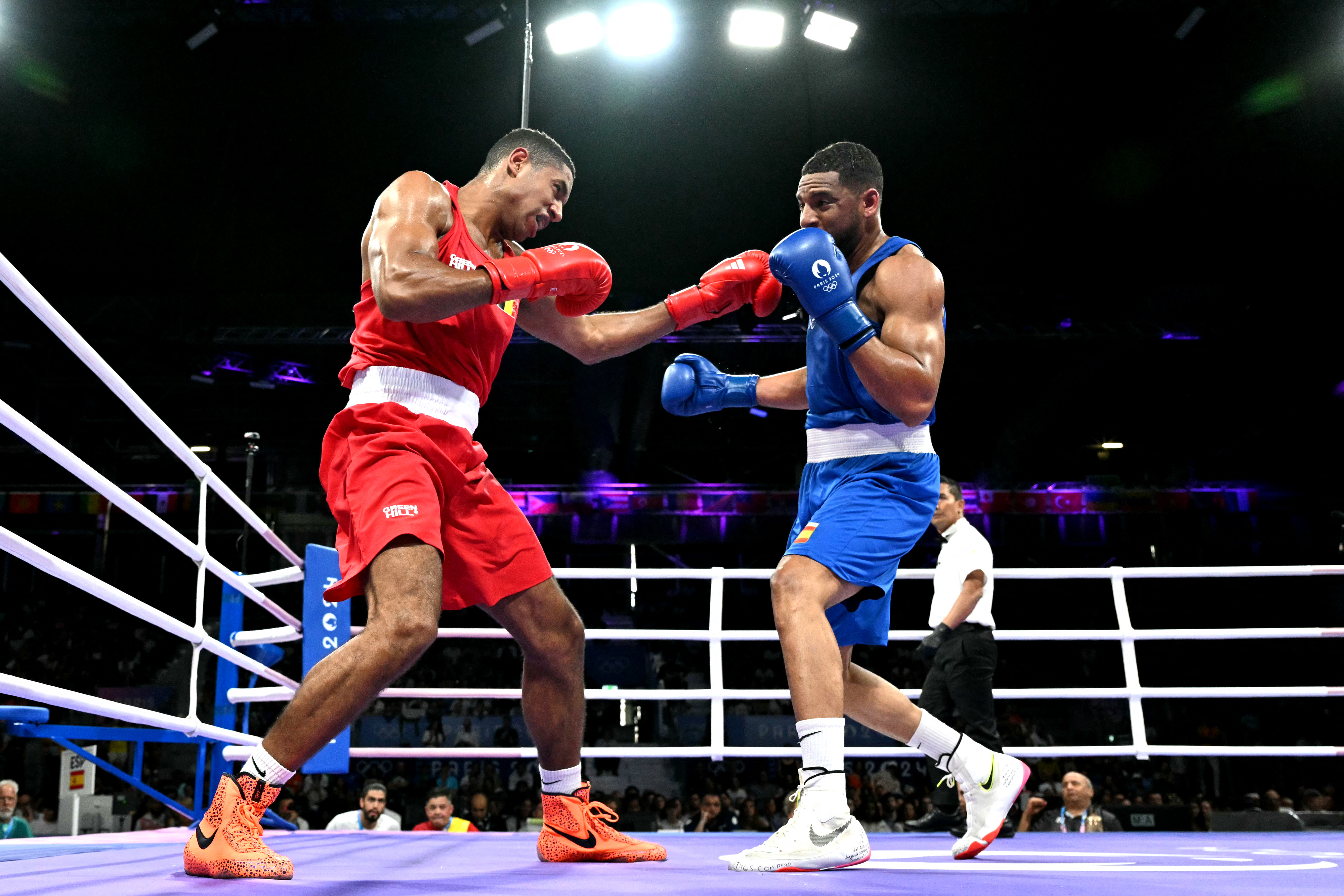 Two boxers in a ring mid-match, with one in red and the other in blue, each throwing simultaneous punches. Audience and referee in background