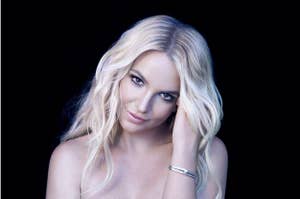 Britney Spears gazes at the camera with her head slightly tilted, her hands touching her hair, and a bracelet on her wrist