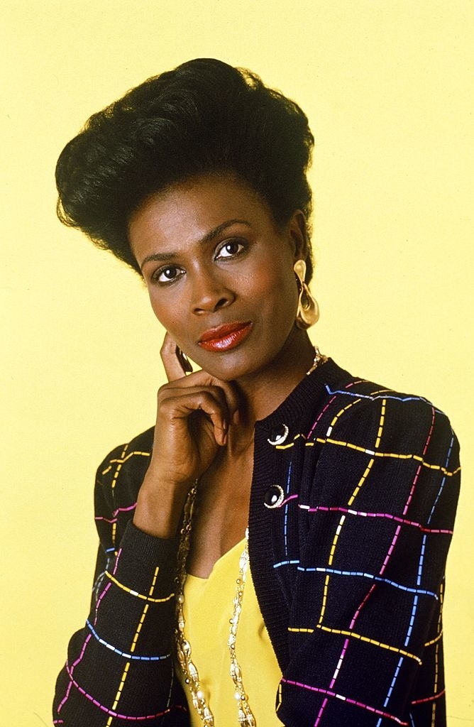 Janet Hubert posing in a patterned jacket and gold earrings against a plain backdrop