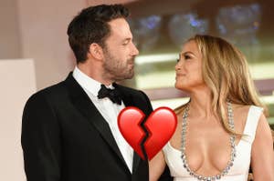 Ben Affleck in a black tuxedo and Jennifer Lopez in a white, plunging neckline dress adorned with sparkling accents, gaze at each other affectionately on the red carpet