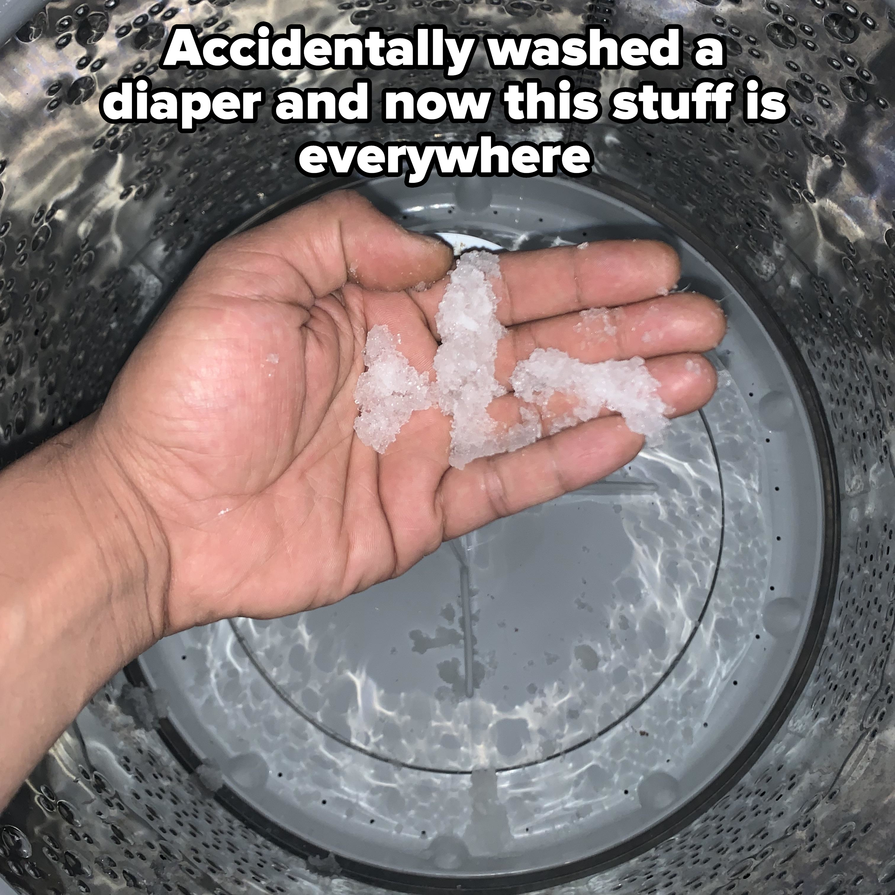 A hand holding chunks of what appears to be ice or salt inside a washing machine