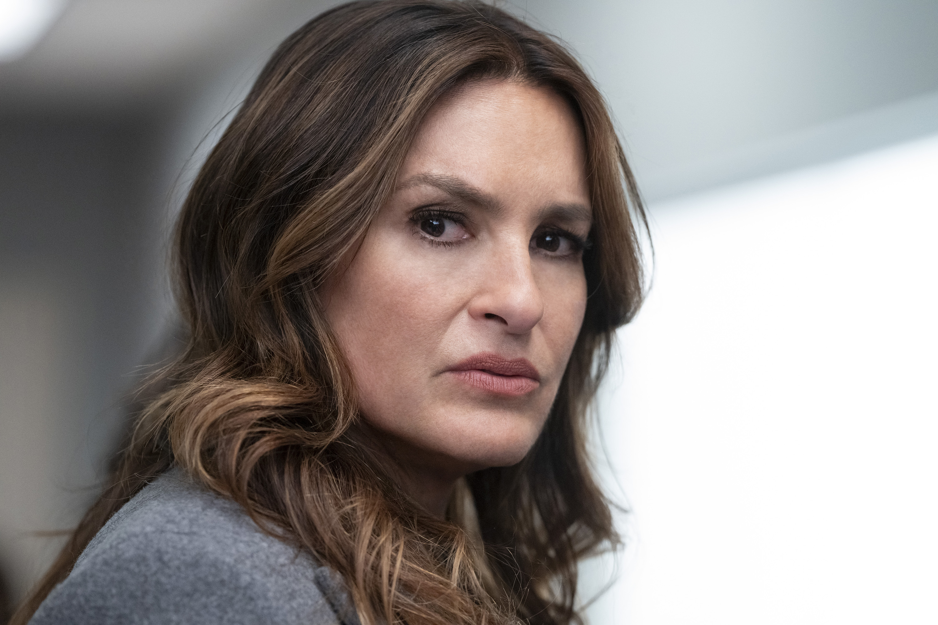 Mariska Hargitay looks serious while gazing toward the camera, with wavy hair cascading over her shoulders in a professional outfit