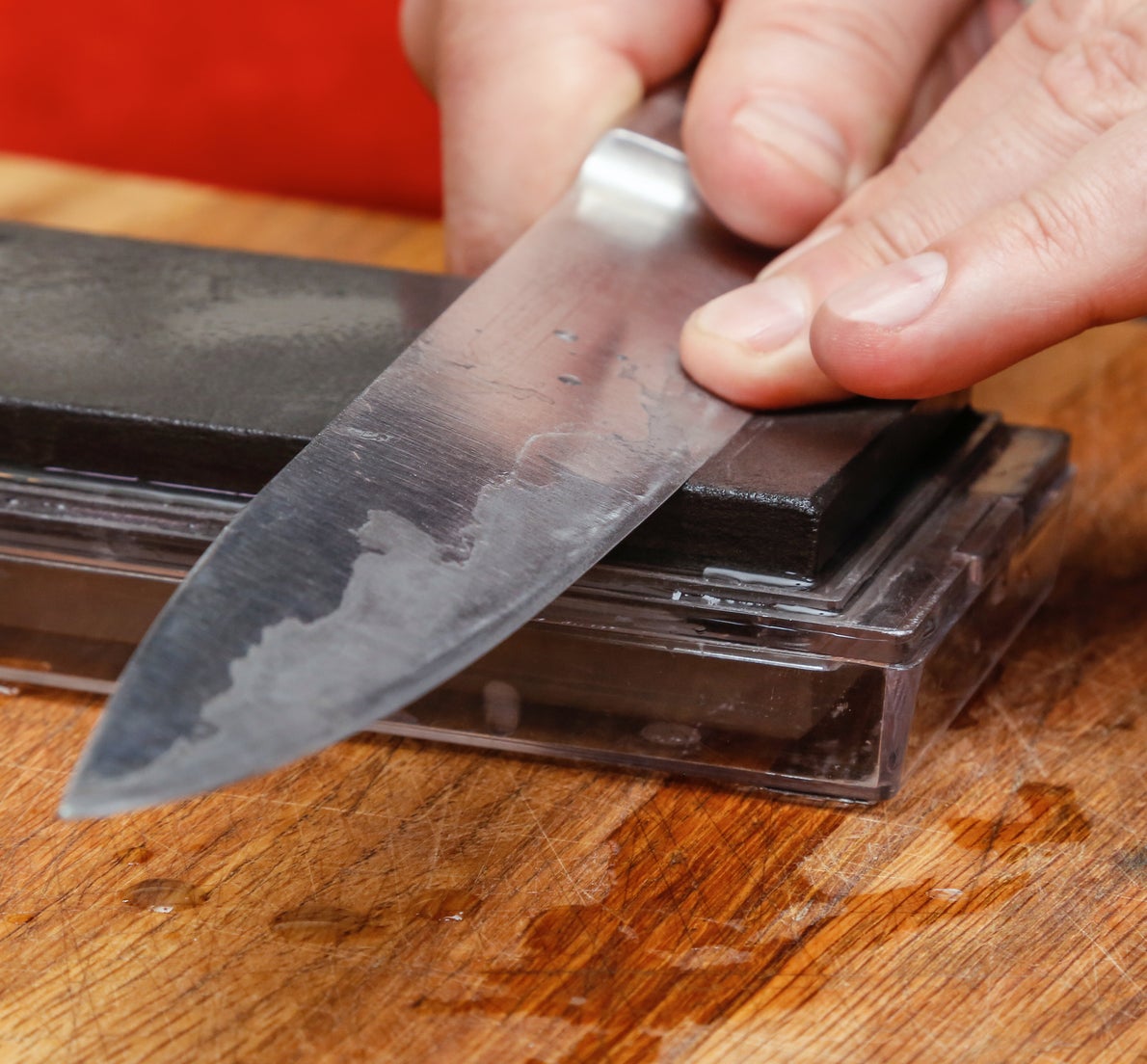 Close-up of hands sharpening a kitchen knife on a whetstone placed on a wooden cutting board