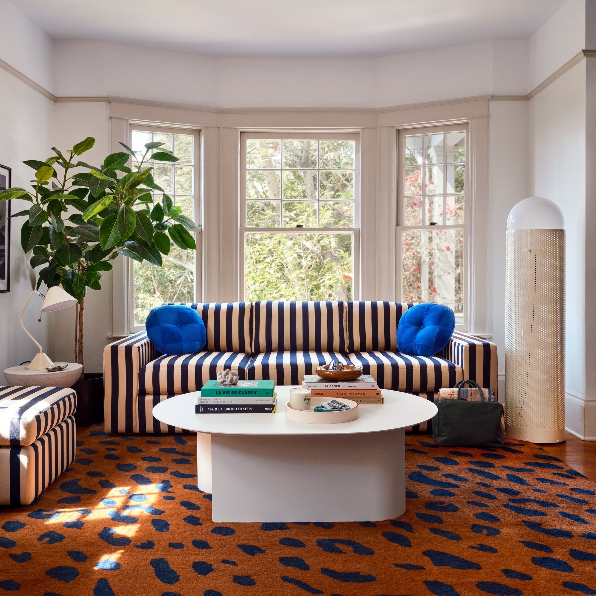 Modern living room with a striped sofa, round white coffee table, and a leopard print rug. Large windows allow natural light to fill the space